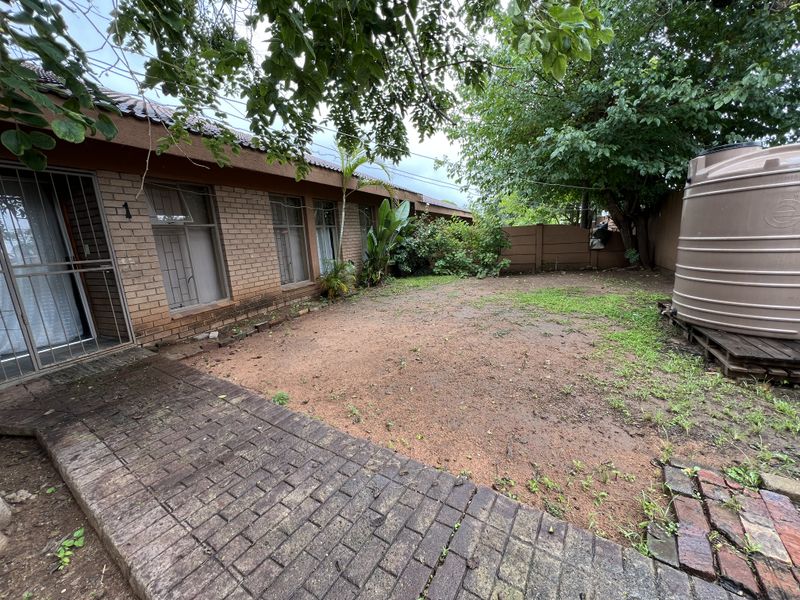 A rear exterior view of the property featuring a brick facade, paved walkway, and a garden area with a large water storage tank.