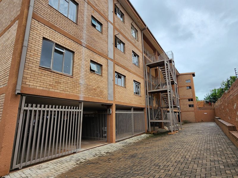 Exterior view of a multi-story apartment building featuring face-brick facade, ground-level secure parking, and external metal staircase access.