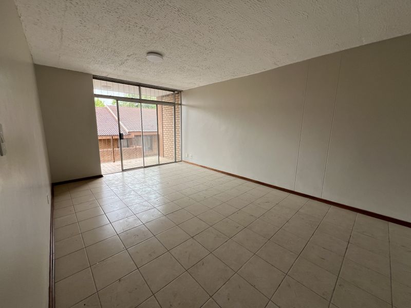 An empty living room featuring tiled flooring, a textured ceiling, and a large sliding glass door providing access to an outdoor patio area.