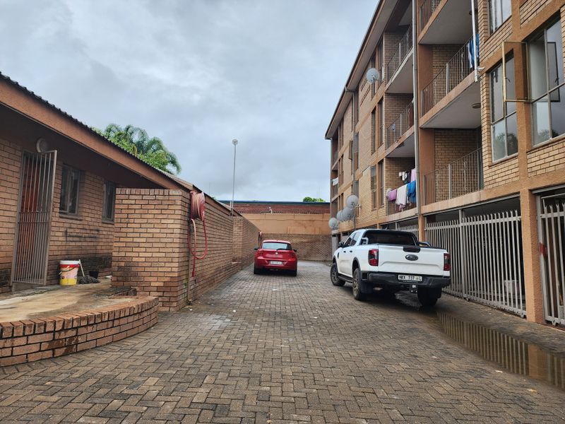 Exterior view of the apartment complex driveway featuring brick facade, paved parking area, and metal security gates.