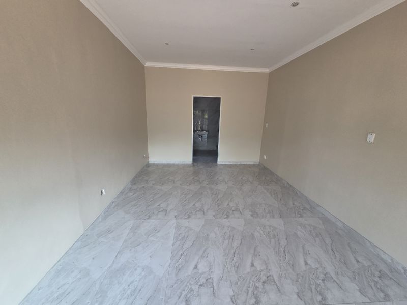 A spacious, empty open-plan retail area featuring modern marble-effect floor tiles, neutral wall finishes, and recessed ceiling lighting with coved cornicing.