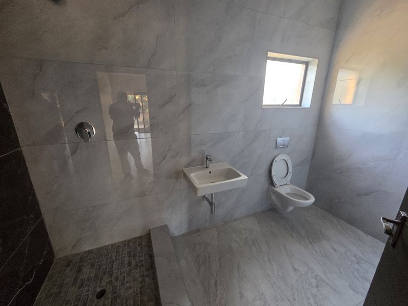 Modern bathroom featuring marble-effect wall tiles, a wall-mounted basin, a wall-hung toilet with a concealed cistern, and a walk-in shower area.