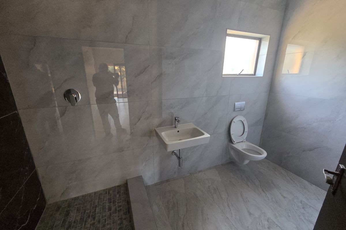 Modern bathroom featuring marble-effect wall tiles, a wall-mounted basin, a wall-hung toilet with a concealed cistern, and a walk-in shower area.