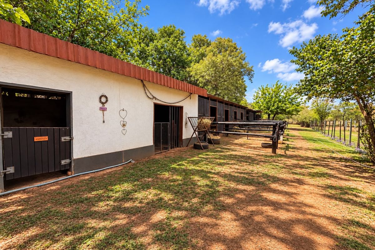 A well-maintained row of stables with metal doors and fencing, situated in a spacious outdoor area on the small holding.