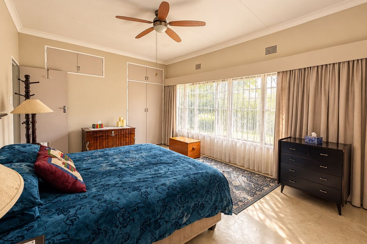 Spacious bedroom featuring built-in cupboards, a ceiling fan, and large windows with security bars, offering a bright and functional living space.