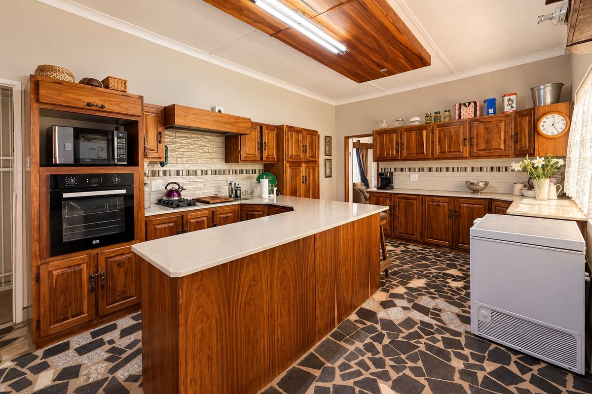 Spacious kitchen featuring warm wooden cabinetry, stone countertops, a built-in oven and microwave, and unique stone mosaic flooring with a feature ceiling panel.