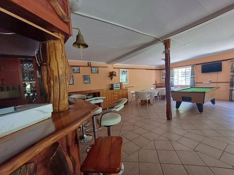 Spacious lodge bar area featuring a rustic built-in wooden bar counter, tiled flooring, and an open-plan layout suitable for entertainment.