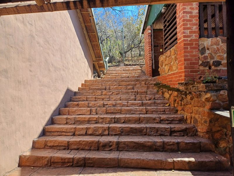 An outdoor stone staircase leading up through the lodge grounds, featuring rustic brick and stone masonry with a thatched roof overhang.