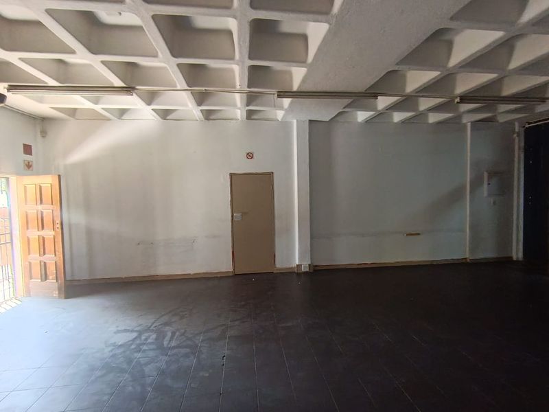 An empty retail space featuring a distinctive waffle-grid concrete ceiling, dark tiled flooring, and a functional layout suitable for various commercial uses.