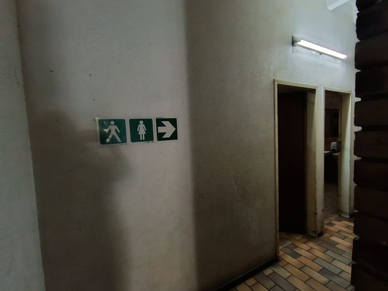 A hallway area featuring directional signage leading to restroom facilities, with tiled flooring and basic wall-mounted lighting.