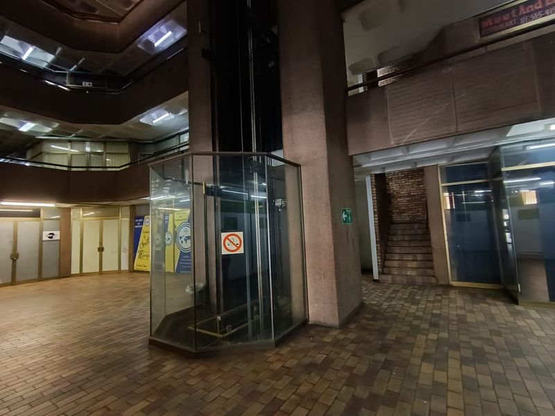 Interior view of a commercial building atrium featuring a central glass elevator, brick flooring, and multi-level access points.