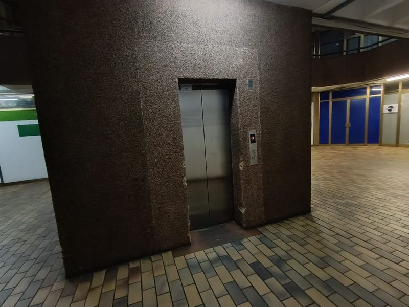Interior view of a commercial building lobby featuring a central elevator unit with textured wall cladding and brick-style floor tiling.