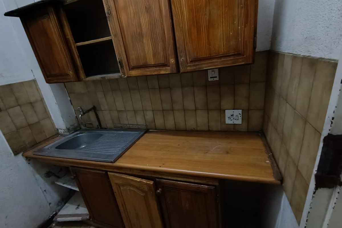 A small, dated kitchenette featuring wooden cabinetry, a stainless steel sink, and tiled splashbacks, requiring significant refurbishment and modernization.