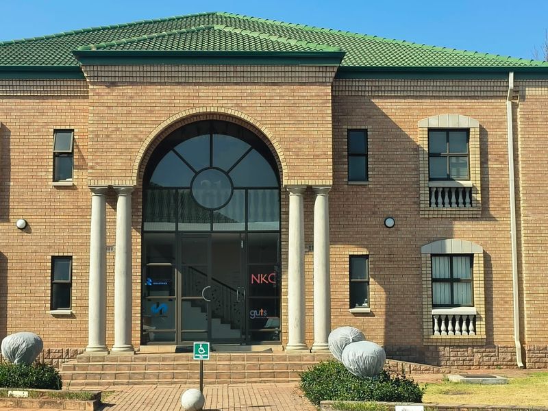 Front elevation of a two-story brick office building featuring an arched glass entrance, stone columns, and decorative balustrades.
