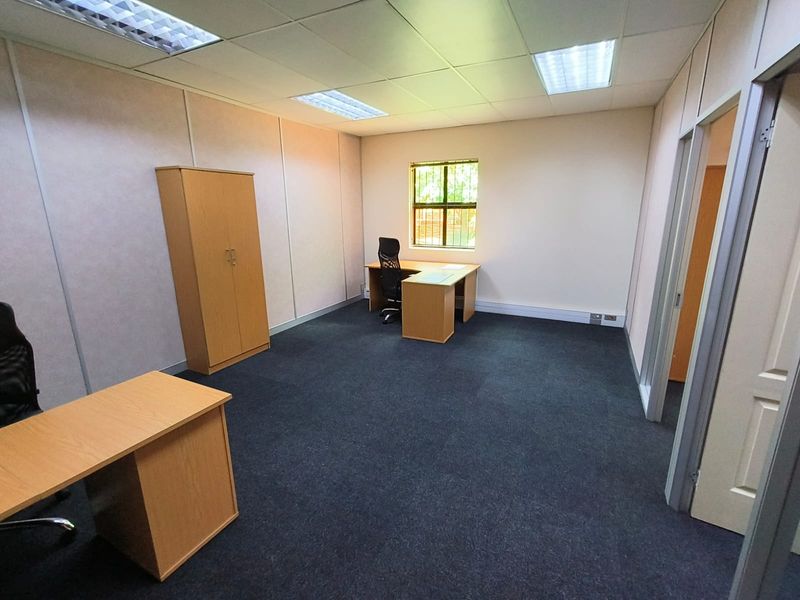 A functional office space featuring a suspended ceiling, recessed lighting, carpeted flooring, and a window with security bars.