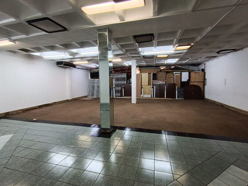 Open-plan retail space featuring a coffered ceiling, mirrored support column, and a combination of tiled and carpeted flooring.