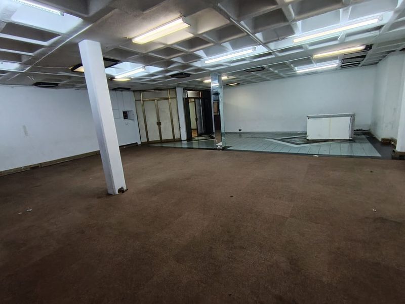 A spacious, open-plan retail area featuring a coffered ceiling, fluorescent lighting, and a mix of carpeted and tiled flooring.