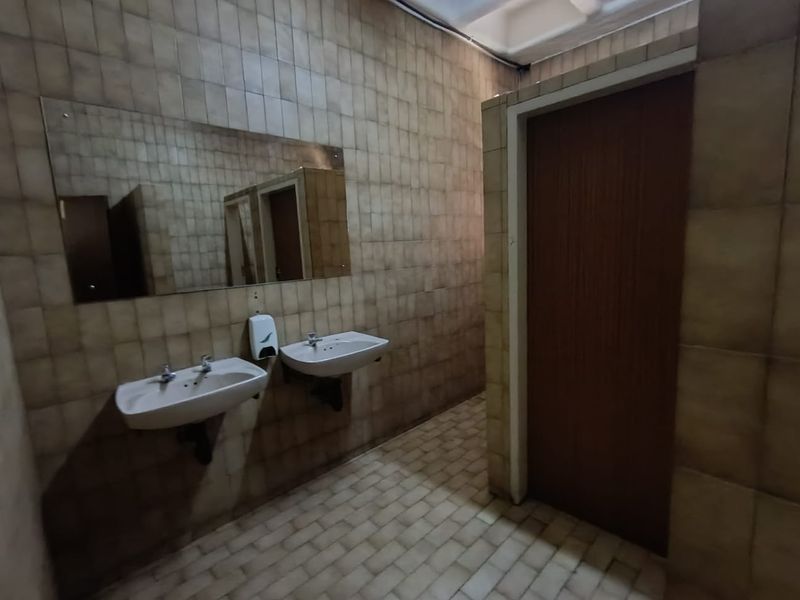 A commercial restroom facility featuring dual wall-mounted ceramic basins, a large vanity mirror, and tiled wall and floor surfaces.