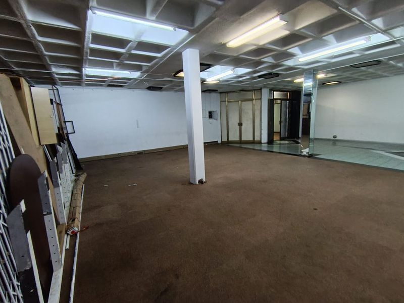 Open-plan retail space featuring a waffle-grid ceiling, central support column, and carpeted flooring, suitable for a variety of commercial business applications.