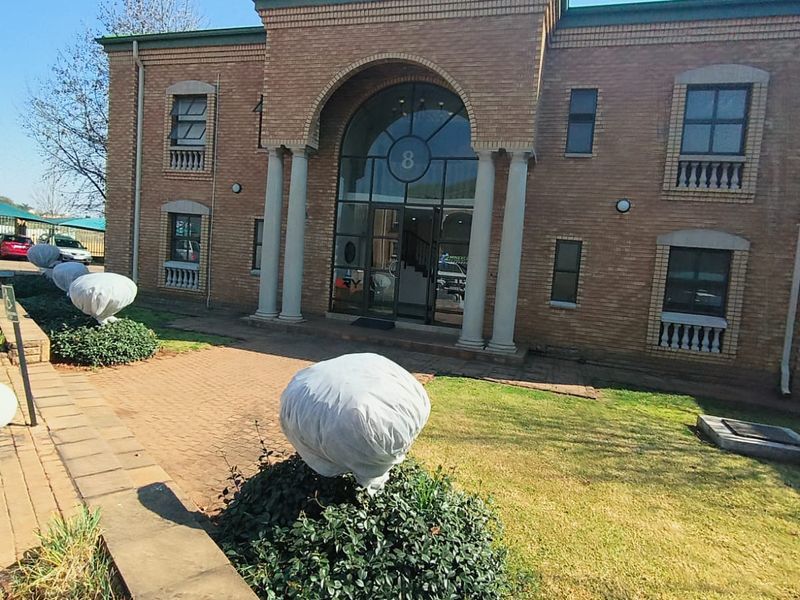 Front exterior view of a two-story brick office building featuring an arched entrance with columns and a paved driveway area.