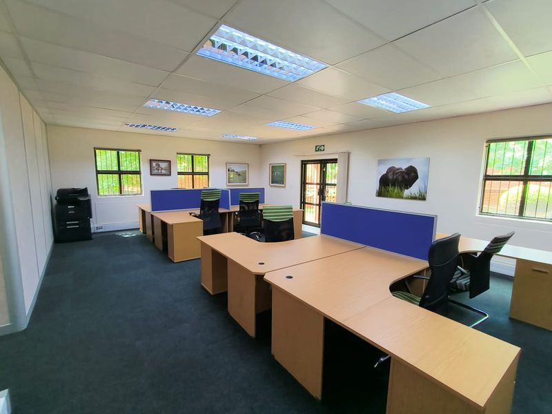 A functional office space featuring suspended ceilings, recessed lighting, and carpeted flooring, equipped with built-in desk partitions and security bars on the windows.