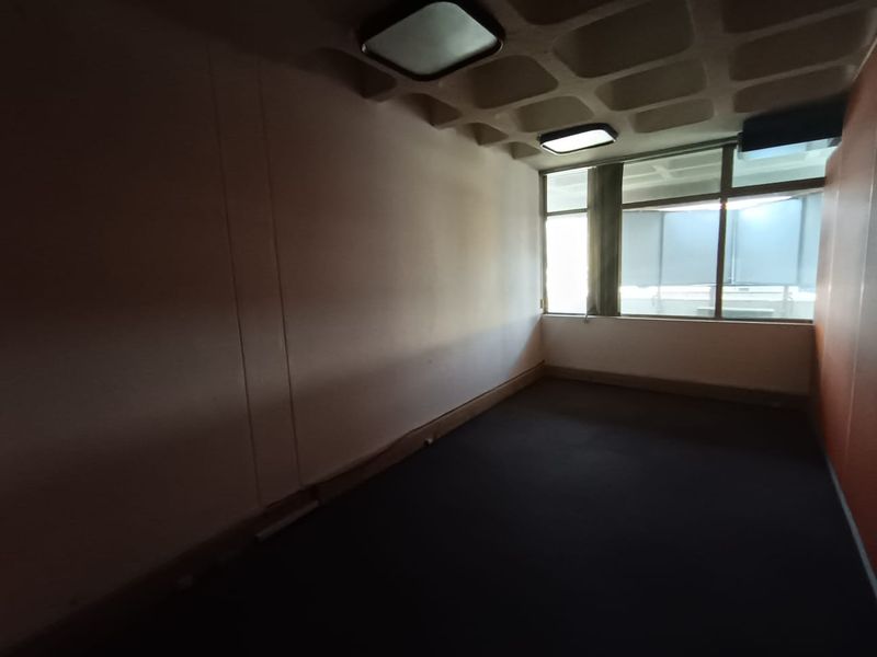An empty office space featuring a waffle-slab concrete ceiling, large windows providing natural light, and dark carpeting.