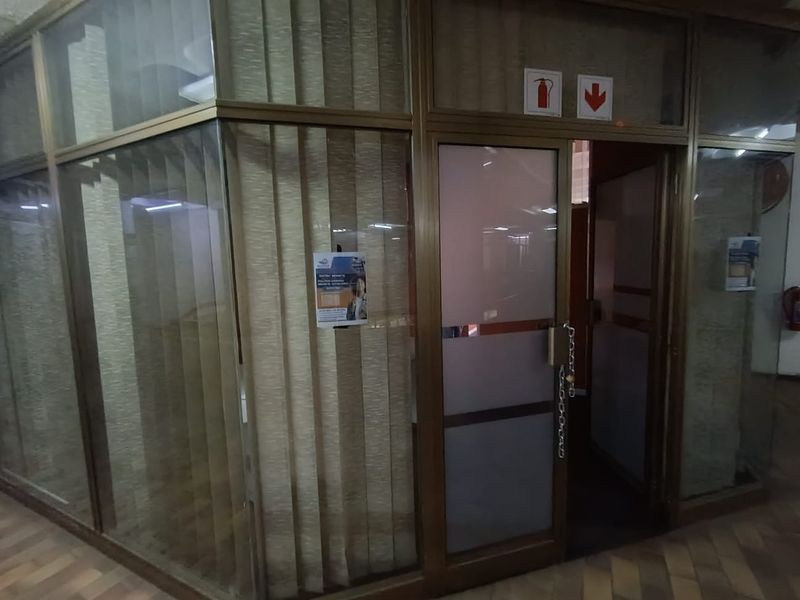 Office entrance featuring a glass-partitioned wall with a secure door, integrated vertical blinds, and safety signage.