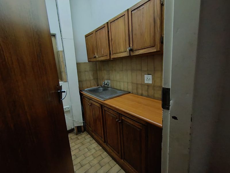 A compact kitchenette featuring wooden cabinetry, a stainless steel sink, and tiled backsplash, suitable for a small office utility area.