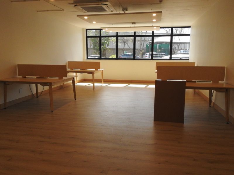 A bright, open-plan office space featuring modern laminate flooring, recessed ceiling lighting, ducted air conditioning, and large windows providing natural light.
