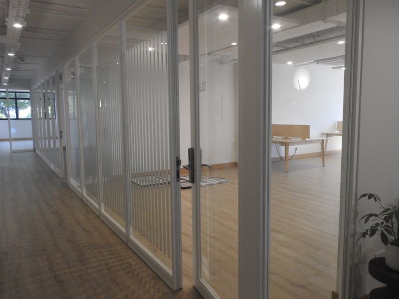 Modern office space featuring glass partition walls, laminate flooring, and recessed lighting, creating a bright and professional work environment.