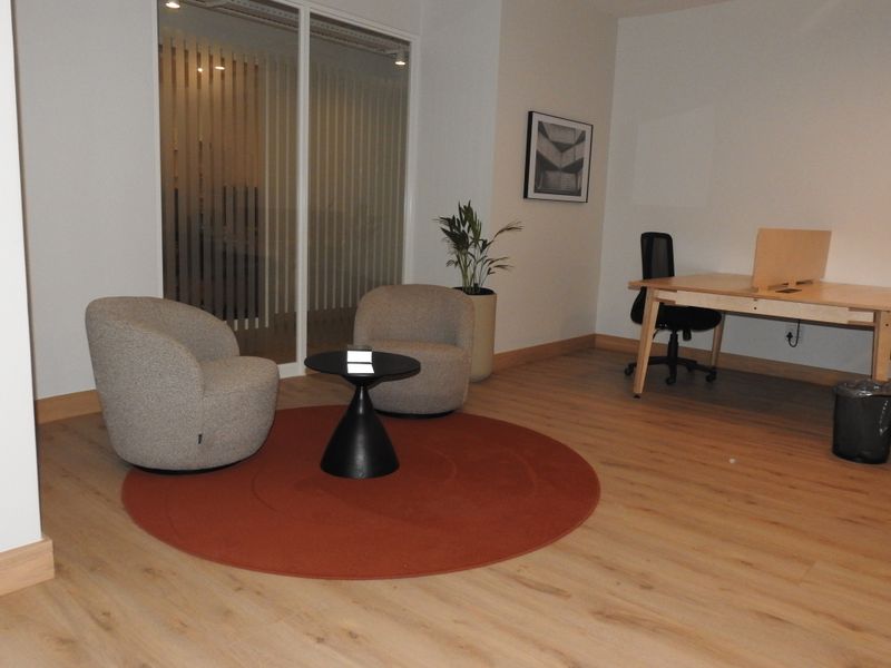 A modern office space featuring light wood-look laminate flooring, a glass partition wall, and clean, neutral wall finishes.