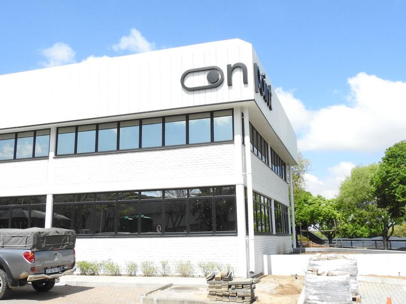 A modern two-story office building featuring white brick and metal cladding, large tinted windows, and a paved exterior area.