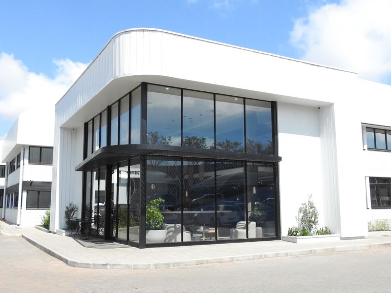 Modern office building exterior featuring a prominent corner glass facade, sleek white metal cladding, and clean architectural lines.