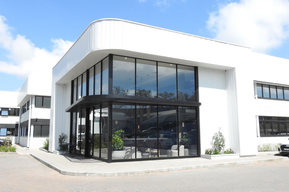 Modern office building exterior featuring a prominent corner glass facade, sleek white metal cladding, and clean architectural lines.