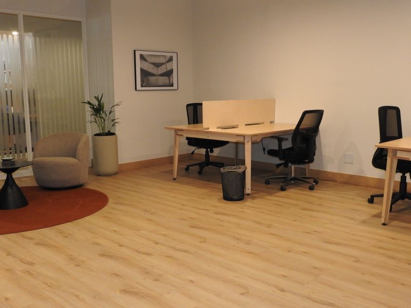 A modern office space featuring light wood-look laminate flooring, neutral walls, and a glass partition wall, providing a clean and professional work environment.