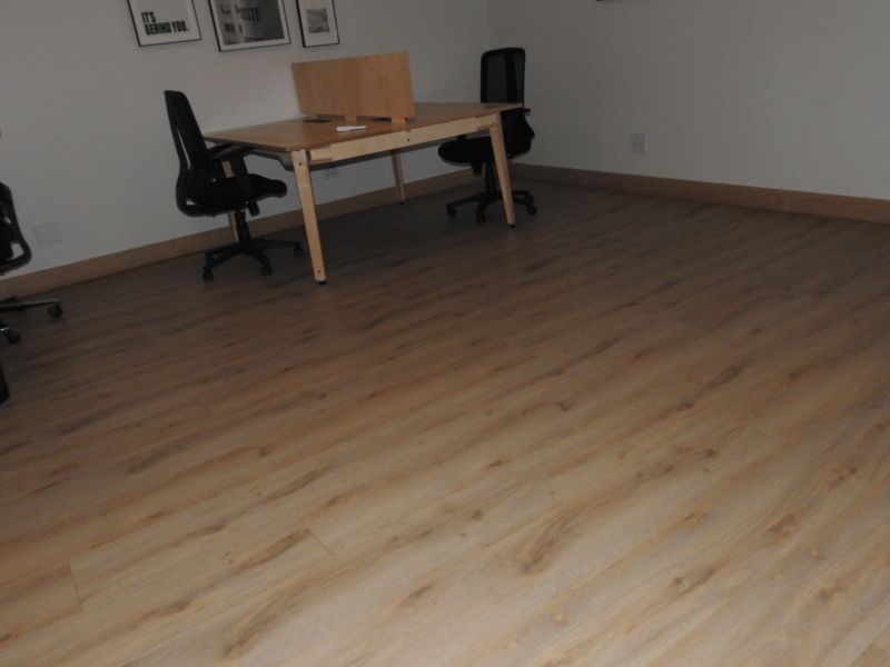 A functional office space featuring modern laminate wood-look flooring and neutral wall finishes, providing a clean and professional work environment.