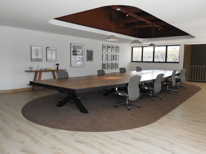 A modern, well-lit office boardroom featuring a large central table, recessed ceiling detail, and contemporary laminate flooring.