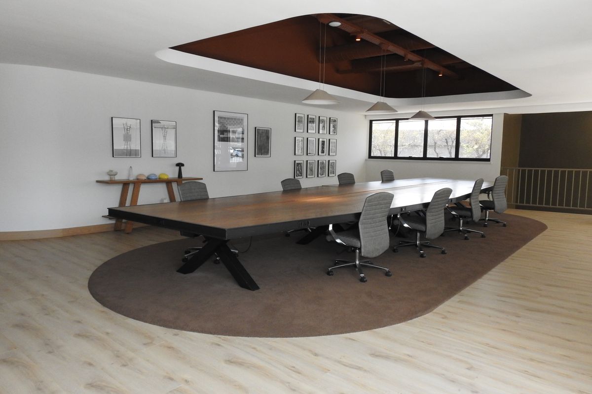A modern, well-lit office boardroom featuring a large central table, recessed ceiling detail, and contemporary laminate flooring.