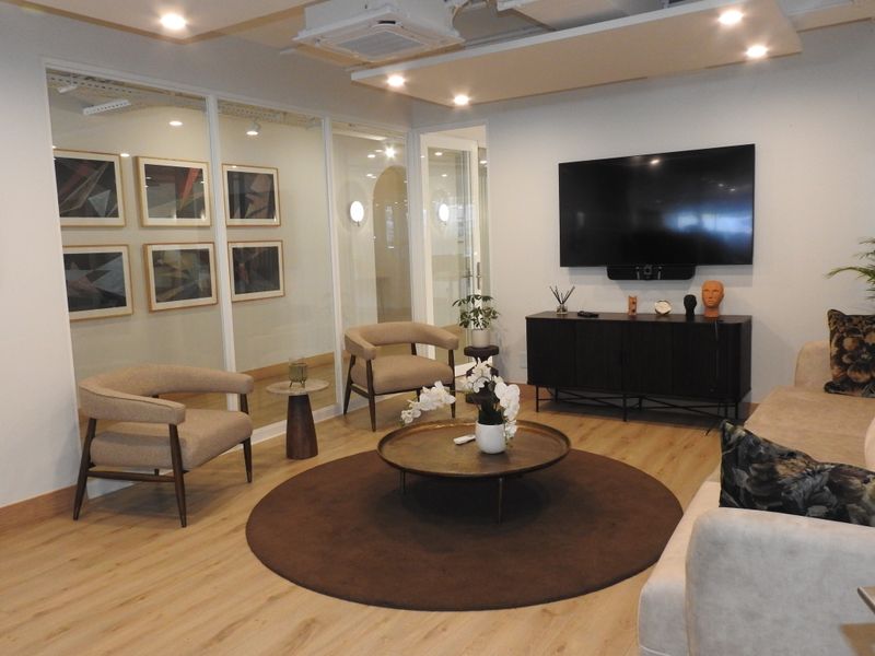 A modern, well-maintained office lounge area featuring laminate wood flooring, recessed ceiling lighting, and a glass partition wall.