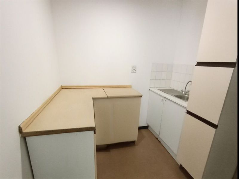 A compact, empty kitchen area featuring laminate countertops, a stainless steel sink with mixer tap, and basic built-in cabinetry with tiled splashback.