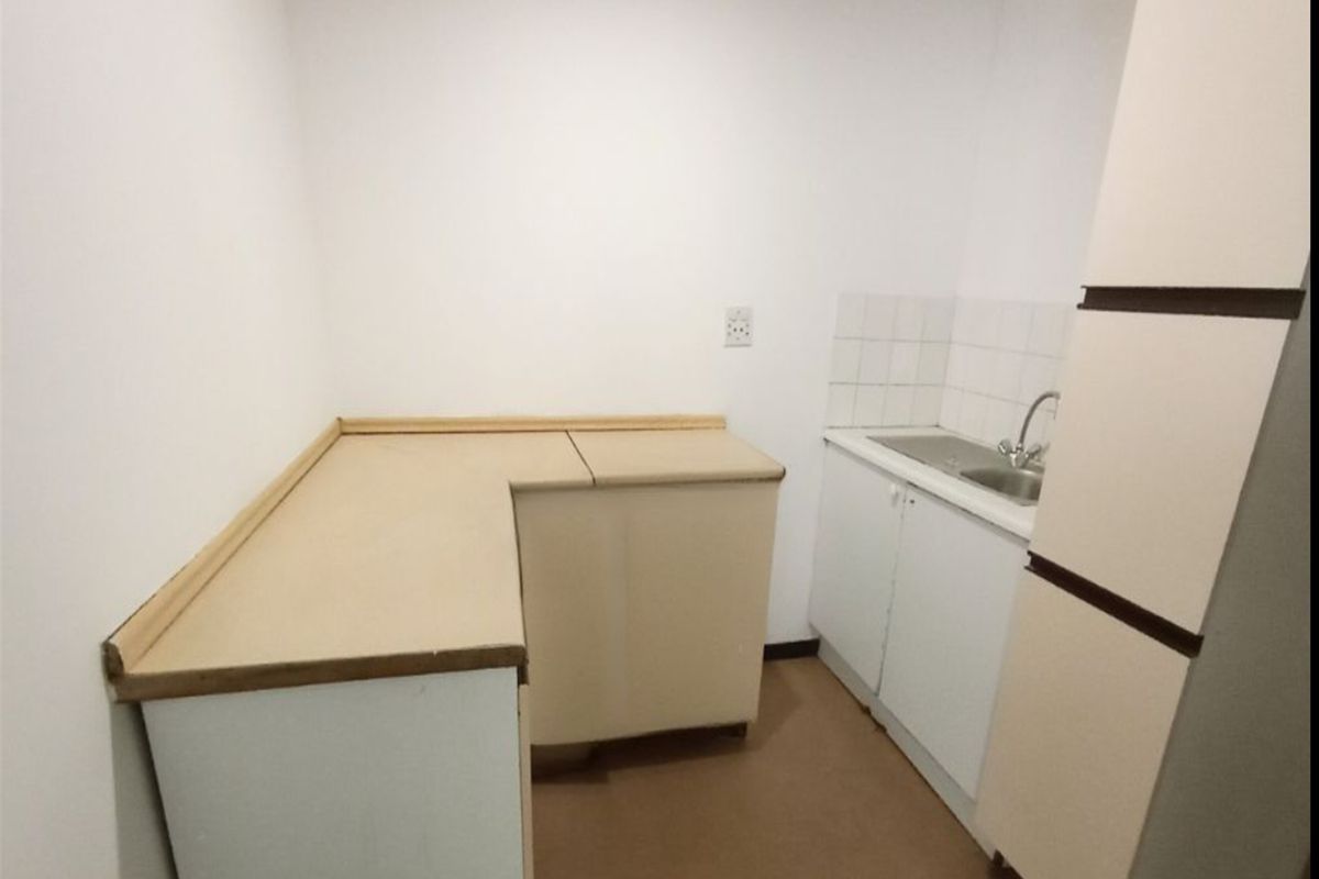 A compact, empty kitchen area featuring laminate countertops, a stainless steel sink with mixer tap, and basic built-in cabinetry with tiled splashback.