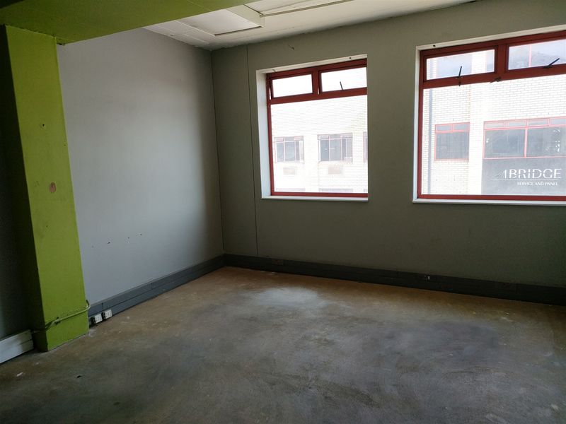 An empty industrial office space featuring exposed concrete flooring, a painted structural column, and large windows providing natural light.