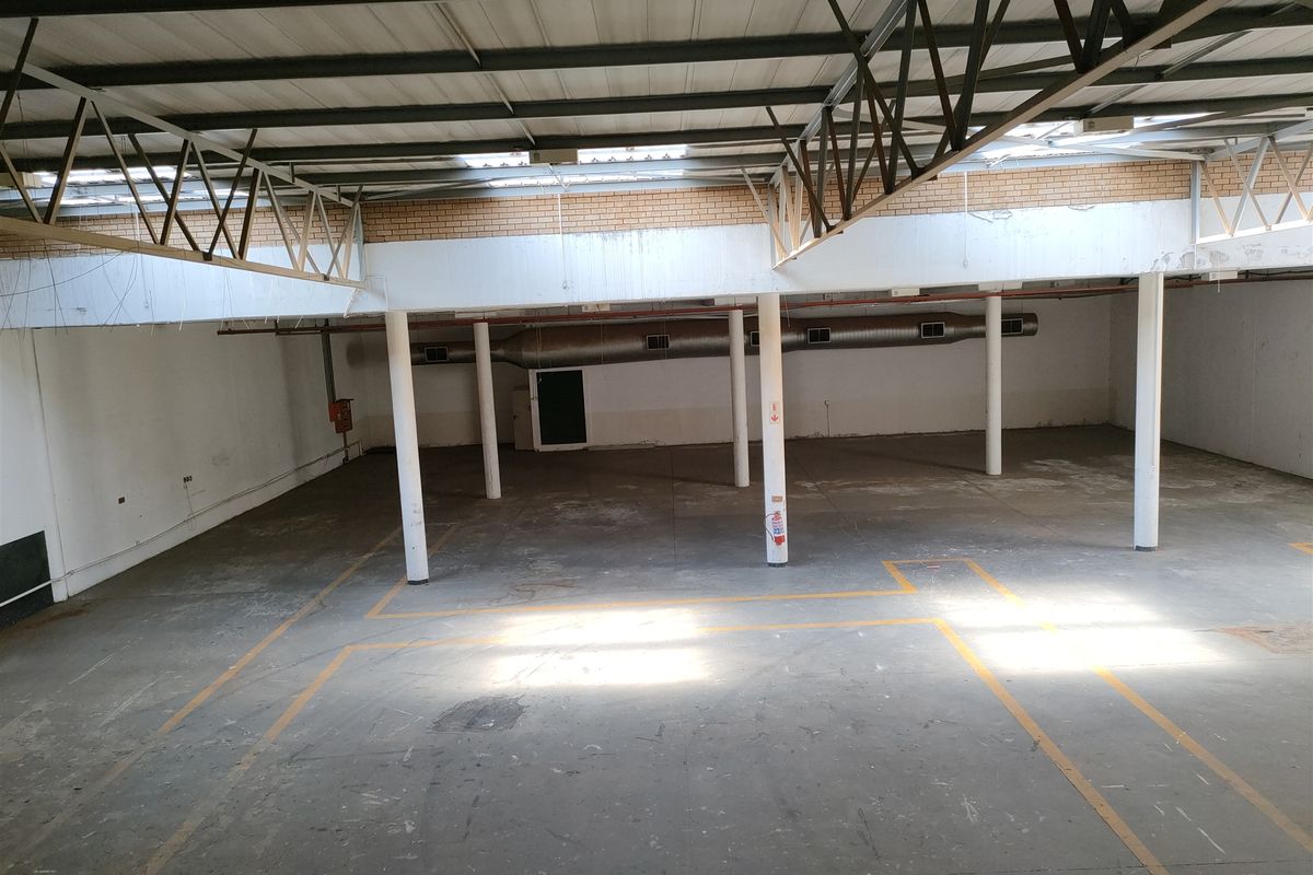 Spacious industrial warehouse area featuring exposed steel roof trusses, concrete flooring, and functional ventilation ducting, suitable for various commercial or storage applications.