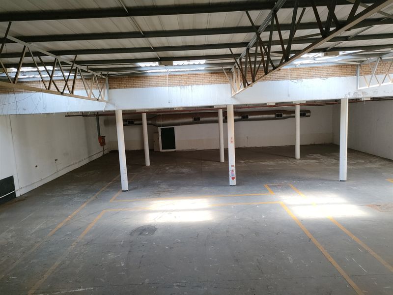 Spacious industrial warehouse area featuring exposed steel roof trusses, concrete flooring, and functional ventilation ducting, suitable for various commercial or storage applications.