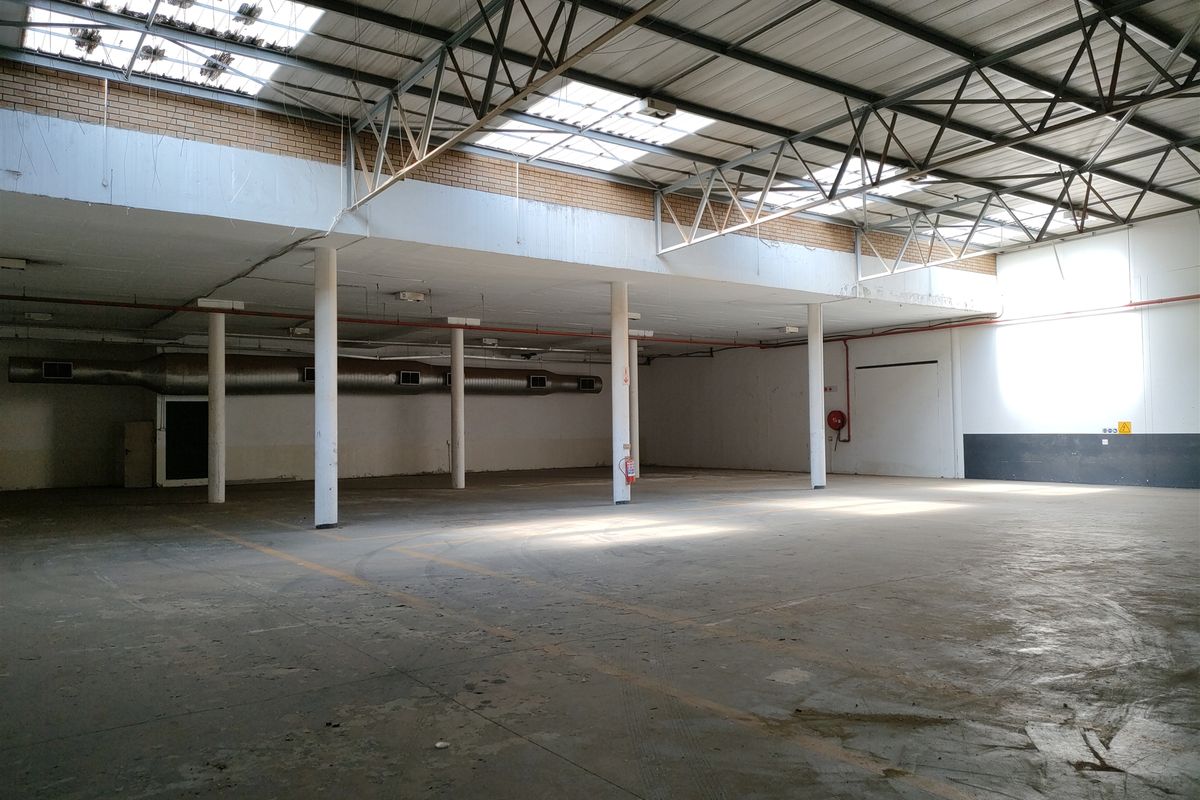 Spacious industrial warehouse area featuring exposed steel roof trusses, skylights, concrete flooring, and functional ventilation ducting, suitable for various commercial or storage applications.