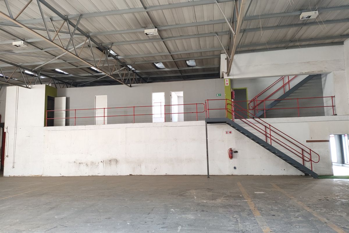 Spacious industrial warehouse interior featuring a mezzanine level with metal staircase, exposed steel roof trusses, skylights, and durable concrete flooring.
