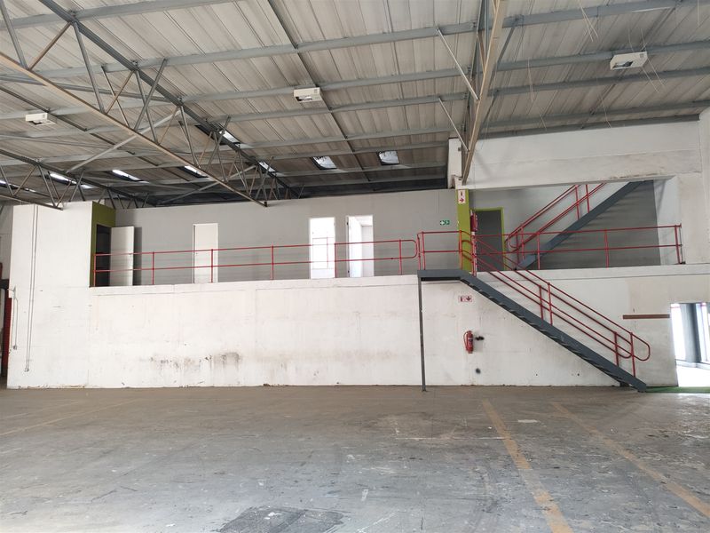 Spacious industrial warehouse interior featuring a mezzanine level with metal staircase, exposed steel roof trusses, skylights, and durable concrete flooring.