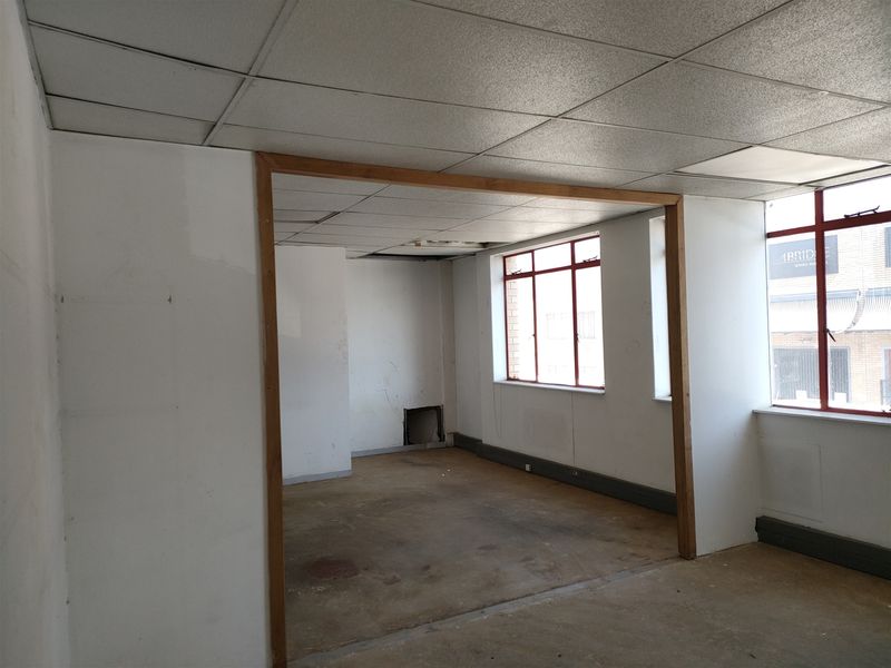 An empty, industrial-style office space featuring a suspended ceiling, large windows with metal frames, and worn flooring, ready for renovation.