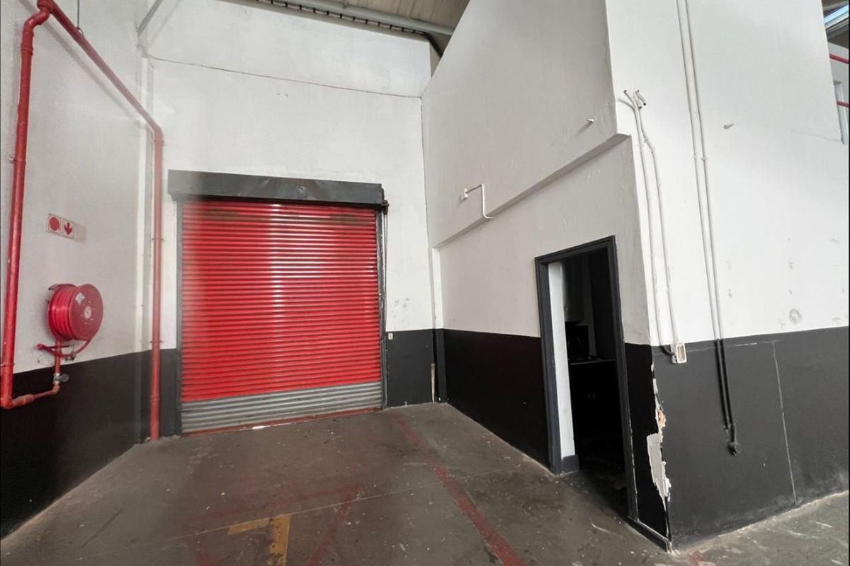 Industrial utility space featuring a red roller shutter door, exposed fire safety infrastructure, and concrete flooring, suitable for storage or logistics operations.