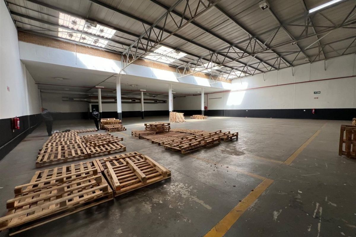 Spacious industrial warehouse featuring high ceilings with exposed steel trusses, natural light from skylights, and durable concrete flooring suitable for various commercial operations.